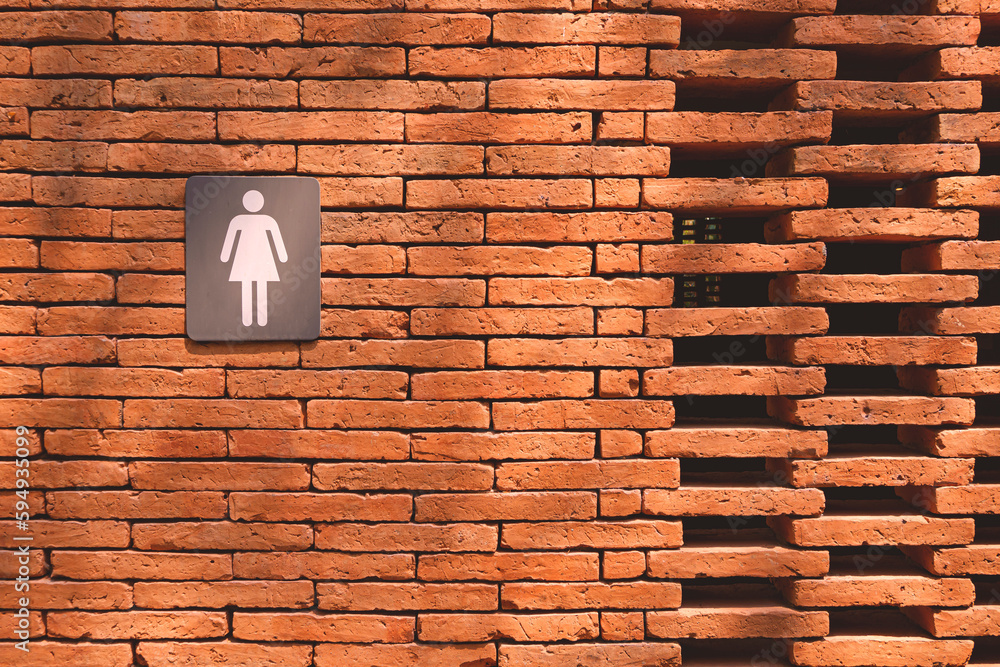Outdoors public restroom with female toilet sign and air vents on brick