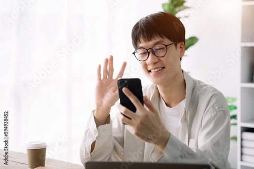 happy smiling Asian student wearing headphones talking on online chat meeting using laptop in university campus or at virtual office. College male student learning remotely. © NINENII