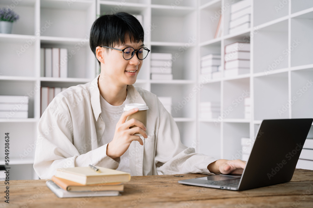 Fototapeta premium male student in casual clothes sitting at wooden table with laptop and writing notes while preparing for exam in library.