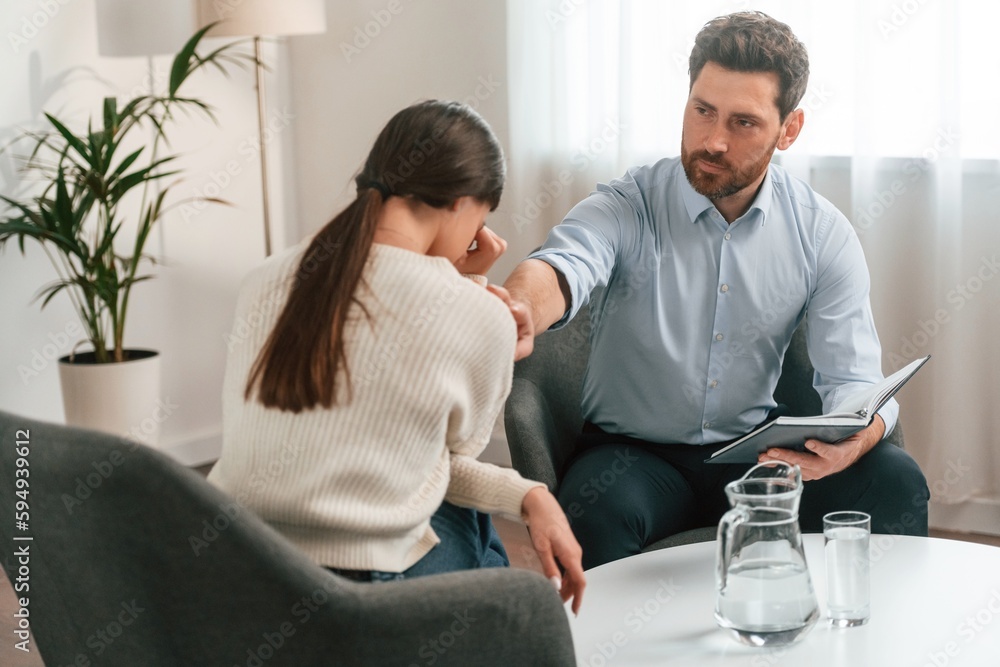 Woman is crying on the therapy session. Doctor in formal clothes is working in the cabinet Woman is crying on the therapy session. Doctor in formal clothes is working in the cabinet