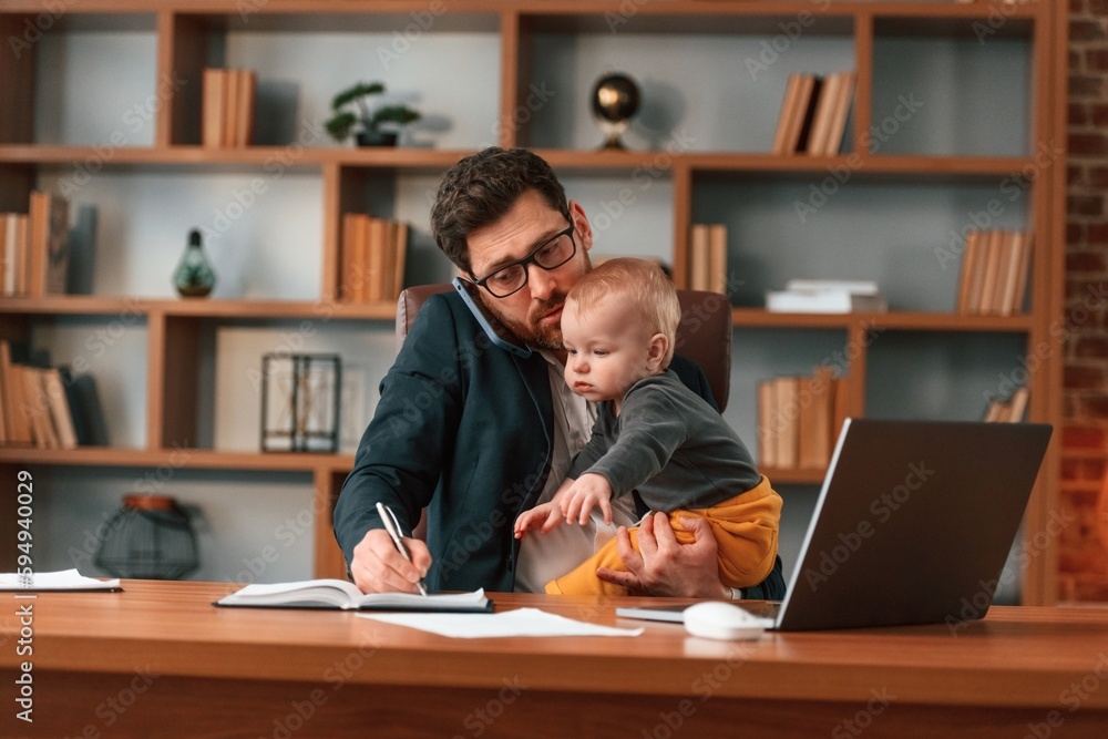 Work and family. Businessman in formal clothes is indoors. With toddler Work and family. Businessman in formal clothes is indoors. With toddler