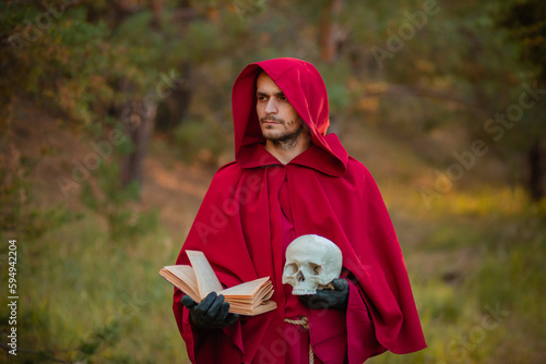 A sorcerer in red clothes with a skull and a book in his hands reads a spell. Medieval monk reads a prayer.