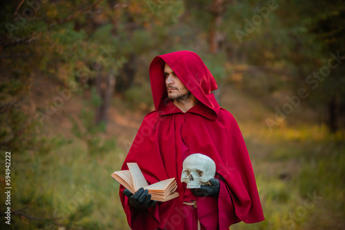 A sorcerer in red clothes with a skull and a book in his hands reads a spell. Medieval monk reads a prayer.