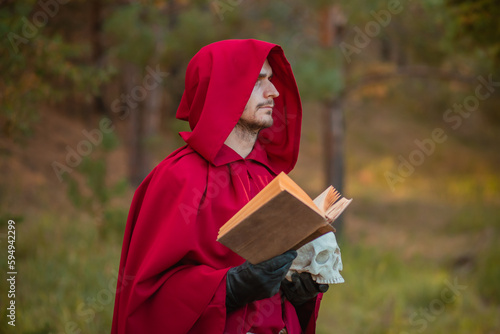 Fototapeta A sorcerer in red clothes with a skull and a book in his hands reads a spell