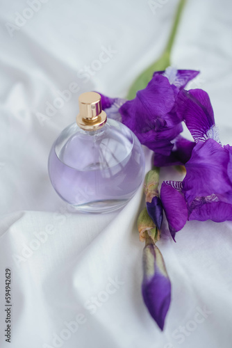 Purple iris flowers and perfume bottle on white fabric background.