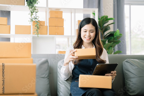 Shipping shopping online ,woman start up small business owner writing address on cardboard box at workplace.small business entrepreneur SME or freelance asian woman working with box at home. © NINENII