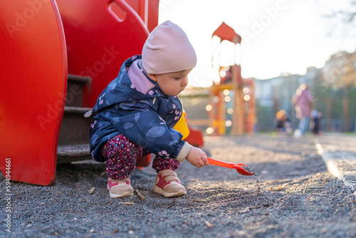 The child is using a children's shovel while playing with sand on the playground. A little girl playing at the playground outdoors. Outdoor creative activities for kids.