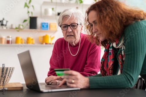 Crop smiling elderly mother and mature daughter using computer while shopping online and paying with plastic card photo