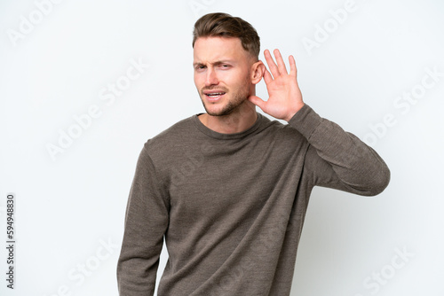 Young blonde caucasian man isolated on white background listening to something by putting hand on the ear