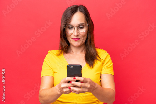 Middle-aged caucasian woman isolated on red background sending a message with the mobile