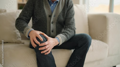 Senior man keeping knee feeling pain sitting on couch at home. Problems with joints, traumas in elderly people. Older male patient knee problem feel painful suffer in injured leg. Health care concept. photo