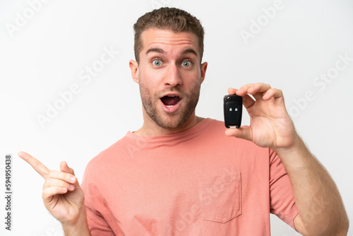 Young caucasian man holding car keys isolated on white background surprised and pointing finger to the side