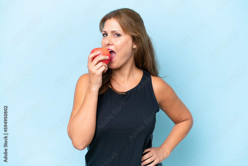 Middle-aged caucasian woman isolated on blue background eating an apple
