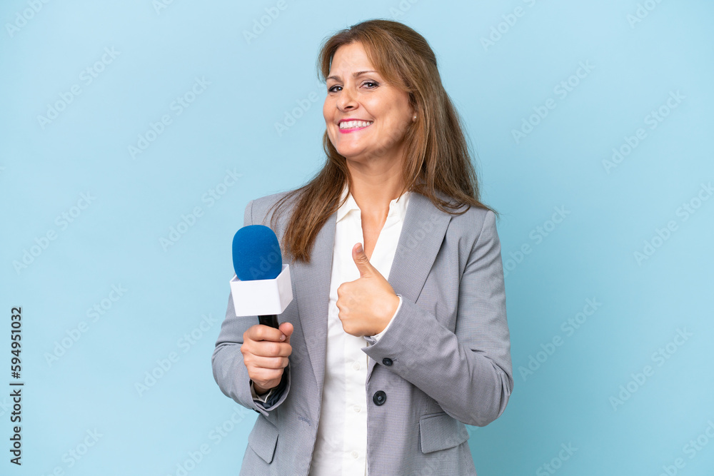 Middle-aged TV presenter woman over isolated blue background giving a thumbs up gesture Middle-aged TV presenter woman over isolated blue background giving a thumbs up gesture