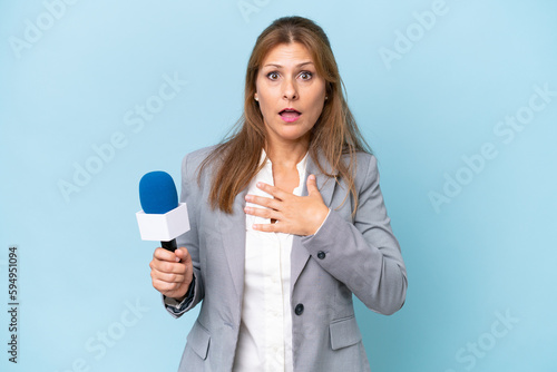Middle-aged TV presenter woman over isolated blue background surprised and shocked while looking right