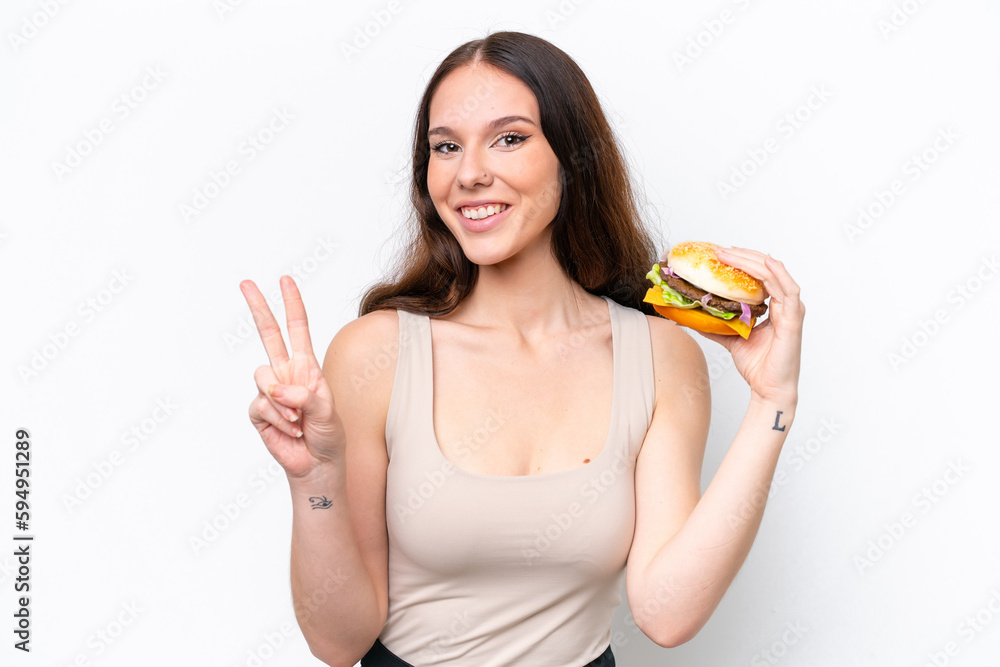 Young caucasian woman holding a burger isolated on white background smiling and showing victory sign Young caucasian woman holding a burger isolated on white background smiling and showing victory sign