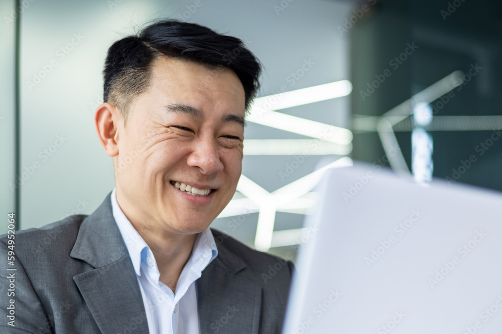 Closeup of cheerful and successful businessman smiling and looking at laptop screen, successful asian boss entrepreneur inside office at workplace looking at laptop screen, reading good news Closeup of cheerful and successful businessman smiling and looking at laptop screen, successful asian boss entrepreneur inside office at workplace looking at laptop screen, reading good news
