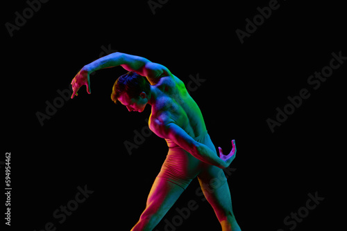 Portrait of young handsome, muscle men, dancer in pastel color clothes posing over dark background with neon light. Demonstrating flexibility © Lustre
