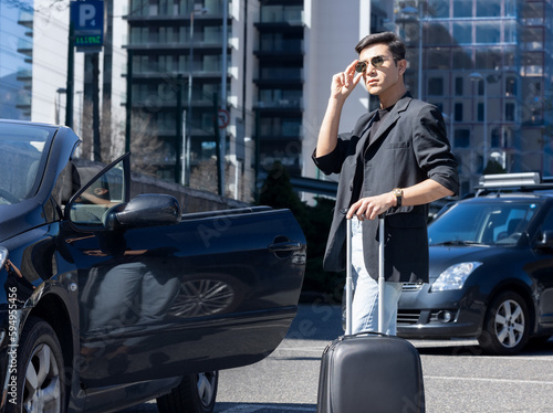 a young man with a suitcase near a car, ready to go in the car, concept of travel for work, car rental, business trip, freelancer © Airiny