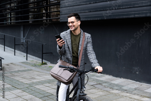 Handsome stylish businessman talking on the phone and driving a bike in the city. Businessperson in front of office building using smartphone on bicycle arrange meeting or date on lunch break