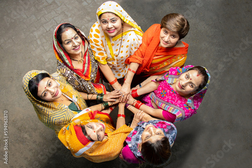 Group of happy young traditional indian women wearing colorful sari looking up while join hands with each other like a team. Rural india. women empowerment. World women's day, Top view photo