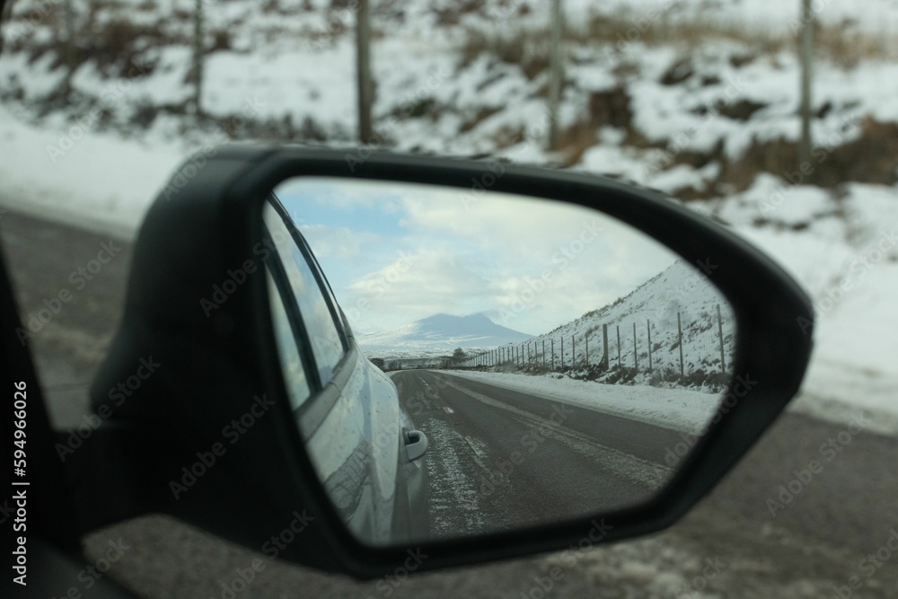 rear view mirror reflecting landscape in mountains on highway during winter
