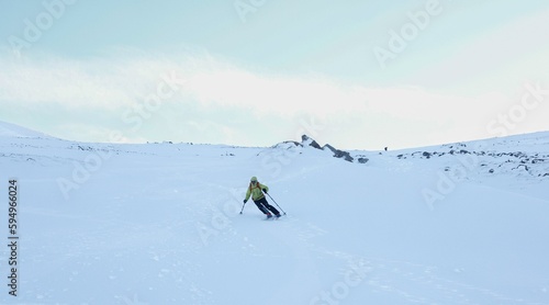 Person wearing a yellow jacket and ski pants skiing down a snow-rcovered mountain slope.