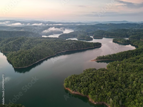 an aerial view of a river surrounded by forest and clouds