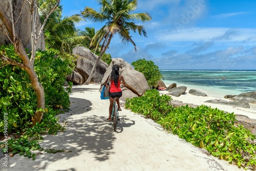 Woman cyclist riding a bicycle along a sandy pathway in tropical beach on La Digue island