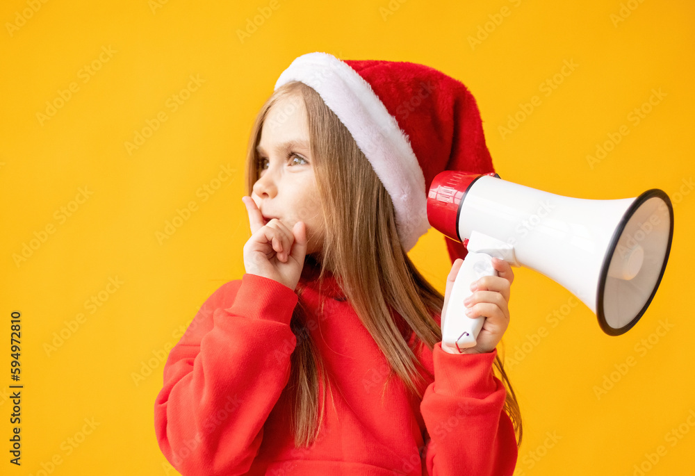 Portrait of a child girl in a Santa hat screaming into a megaphone, color background Portrait of a child girl in a Santa hat screaming into a megaphone, color background