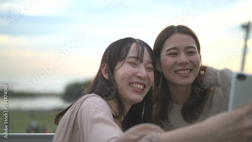 夕暮れの公園でスマートフォンを使ってセルフィーを撮る二人の女性