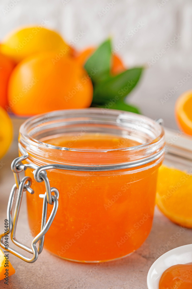 Orange marmalade or orange jam in glass jar with fresh fruits on a gray background. Copy space. Orange marmalade or orange jam in glass jar with fresh fruits on a gray background. Copy space.