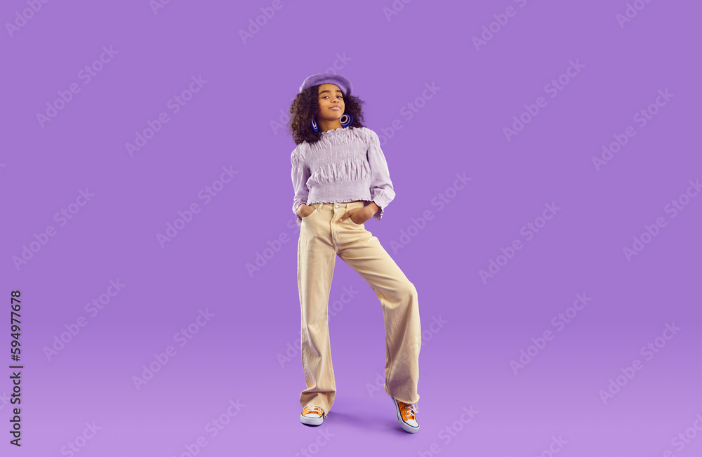 Kid model in stylish fit posing in studio. Full body length beautiful African girl wearing beret hat, blouse and beige wide leg jeans standing on purple background. Clothing, childrens fashion concept Kid model in stylish fit posing in studio. Full body length beautiful African girl wearing beret hat, blouse and beige wide leg jeans standing on purple background. Clothing, childrens fashion concept
