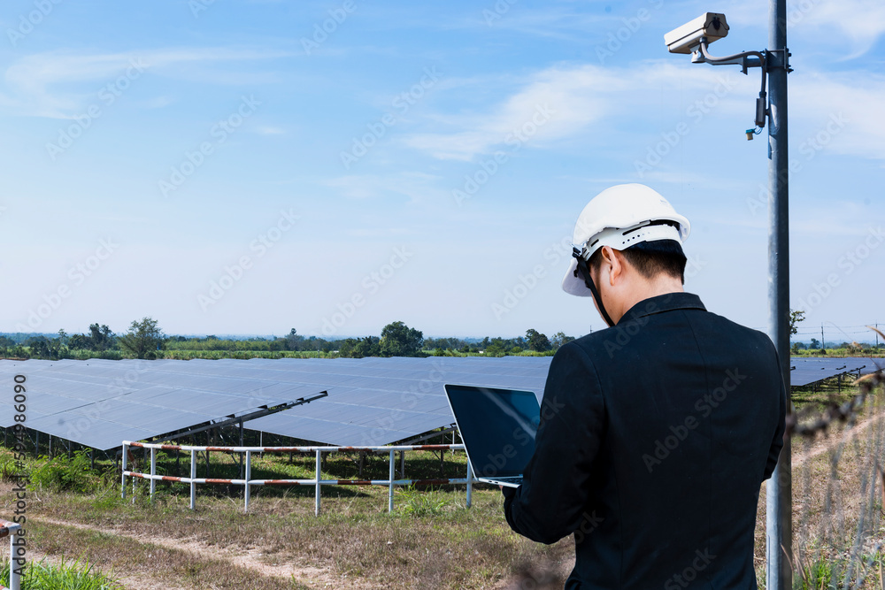 Young man working at solar power station with digital tablet - Renewable energy with wind turbines and solar panels.