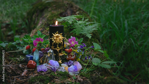 Burning black candle with sun amulet, gemstones, flowers in forest, dark natural abstract background. esoteric ritual for Summer solstice, Midsummer, Litha. pagan witch tradition, wiccan practice
