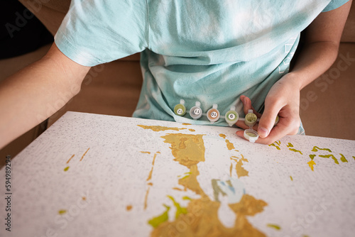 Young male teenager painting picture by numbers on canvas in living room at home. Hobby and leisure concept.