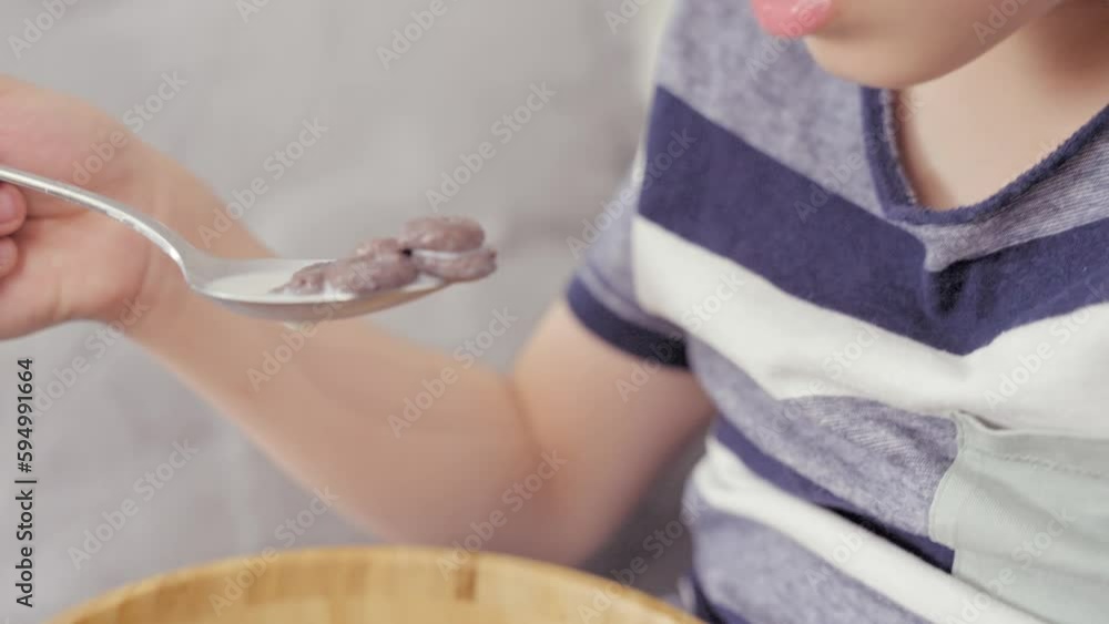 Cute Caucasian little boy eating dry breakfast with milk in wooden bowl, moving camera, close up. Children health and growth concept Cute Caucasian little boy eating dry breakfast with milk in wooden bowl, moving camera, close up. Children health and growth concept