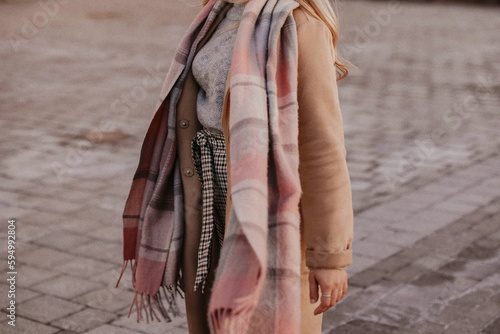 Woman in autumn outfit brown coat and scarf walking in the city. Female casual street style fashion