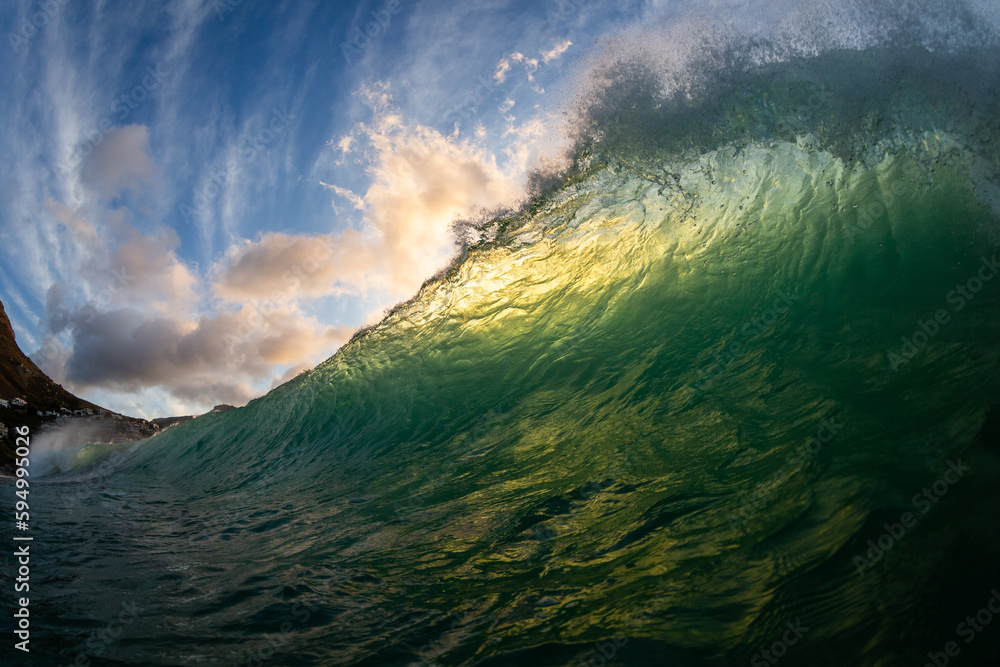 green wave breaking at sunset with dramatic cloud scape