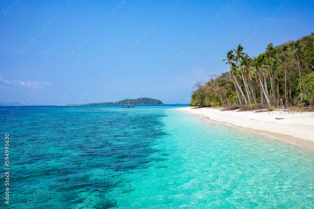 A deserted white beach with palm trees and clear turquoise water on a sunny day with blue skies. A tropical island in Palawan Philippines.