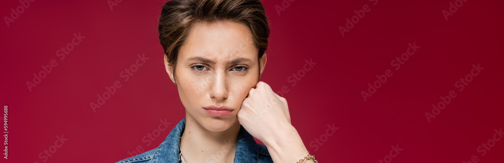 sad young woman with short hair looking at camera on burgundy background, banner. sad young woman with short hair looking at camera on burgundy background, banner.