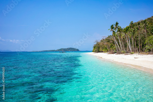 A deserted white beach with palm trees and clear turquoise water on a sunny day with blue skies. A tropical island in Palawan Philippines. © Mirador