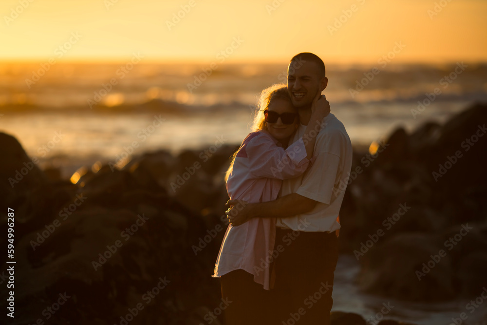 Romantic young couple embracing by the ocean during a golden sunset.