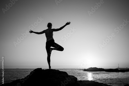 Yoga silhouette female on the oceanfront during a lovely sunset. Black and white photo..