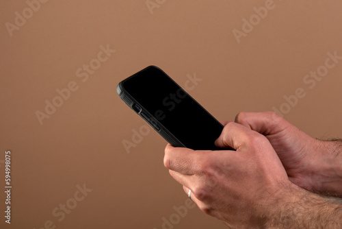 Male hands hold a smartphone on a beige background. Man using smartphone