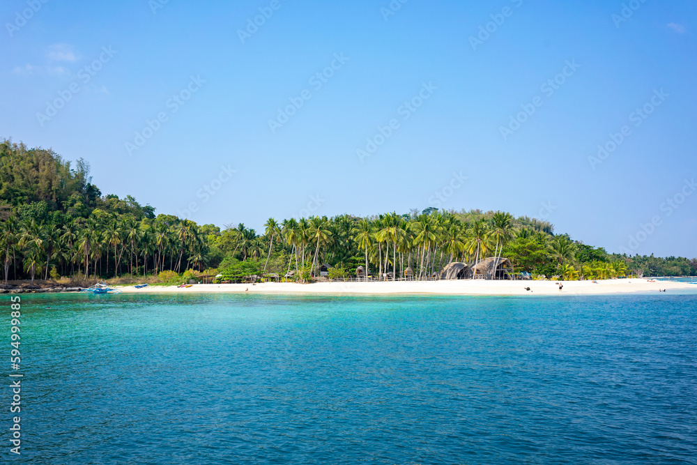 A deserted white beach with palm trees and clear turquoise water on a sunny day with blue skies. A tropical island in Palawan Philippines.
