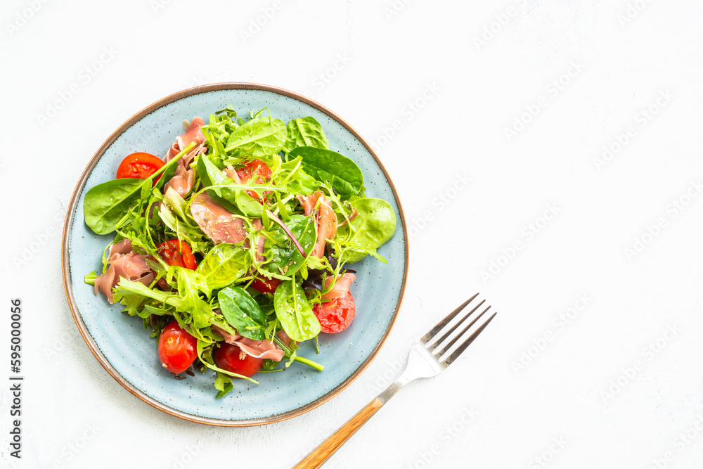 Green salad with fresh leaves, tomatoes and jamon at white table. Top view with copy space. Green salad with fresh leaves, tomatoes and jamon at white table. Top view with copy space.
