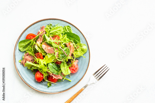 Green salad with fresh leaves, tomatoes and jamon at white table. Top view with copy space.