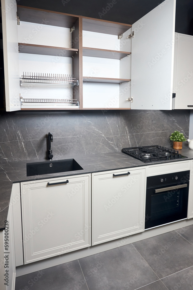 Interior of white and grey kitchen, horizontal linear layout. Luxury modern fitted flat design kitchen with opened cupboard shelves sideboard with dish drying cabinet vertical shot. Interior of white and grey kitchen, horizontal linear layout. Luxury modern fitted flat design kitchen with opened cupboard shelves sideboard with dish drying cabinet vertical shot.