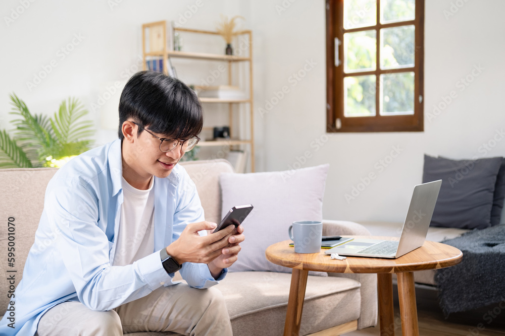 Photo of young cheerful man happy positive smile read browse internet cellphone chat type sms sit couch indoors Photo of young cheerful man happy positive smile read browse internet cellphone chat type sms sit couch indoors